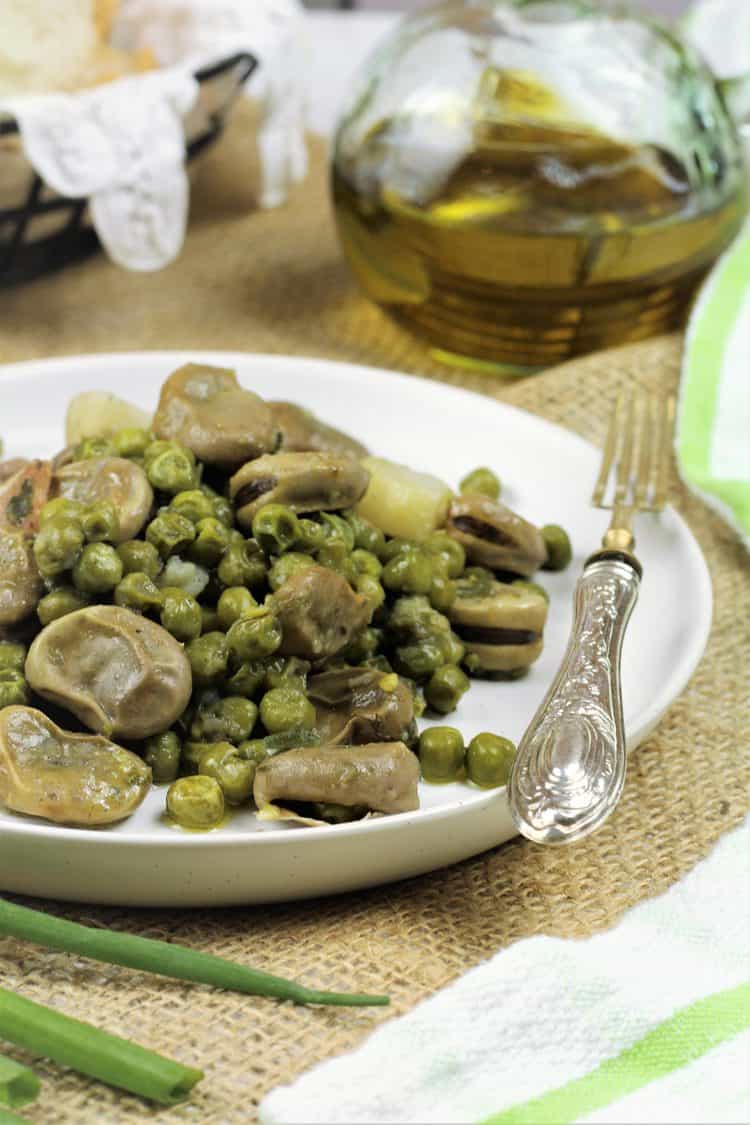 white plate with fava beans and peas with fork on side and olive oil bottle