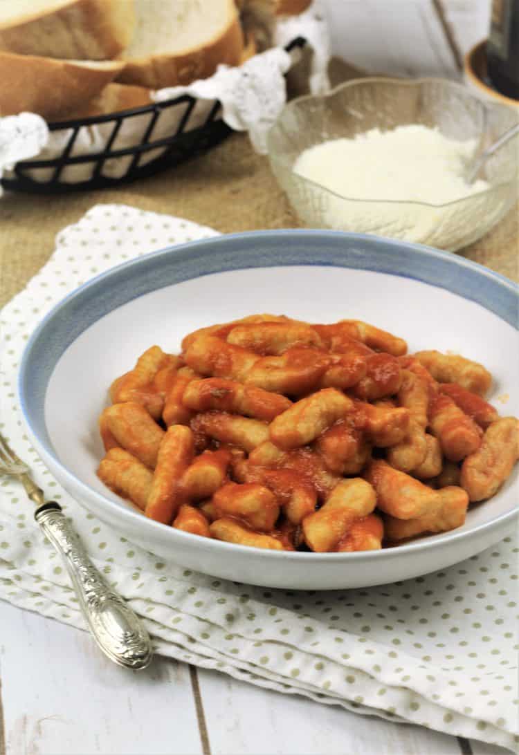 bowl of gnocchi with tomato sauce on polka doted napkin with fork on side and cheese bowl