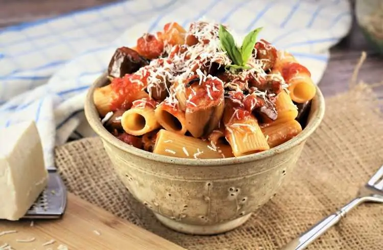 ceramic bowl filled with eggplant pasta topped with cheese 