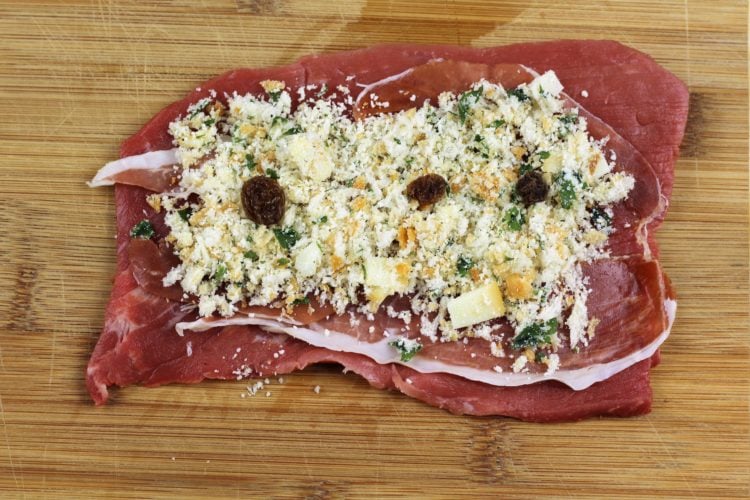 slice of beef braciole topped with breadcrumbs, prosciutto and raisins