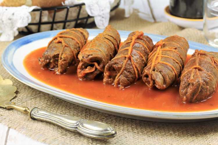 beef braciole tied in butcher's twine on plate with tomato sauce 
