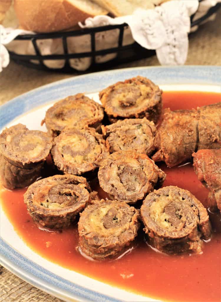 sliced beef braciole rounds on platter with tomato sauce