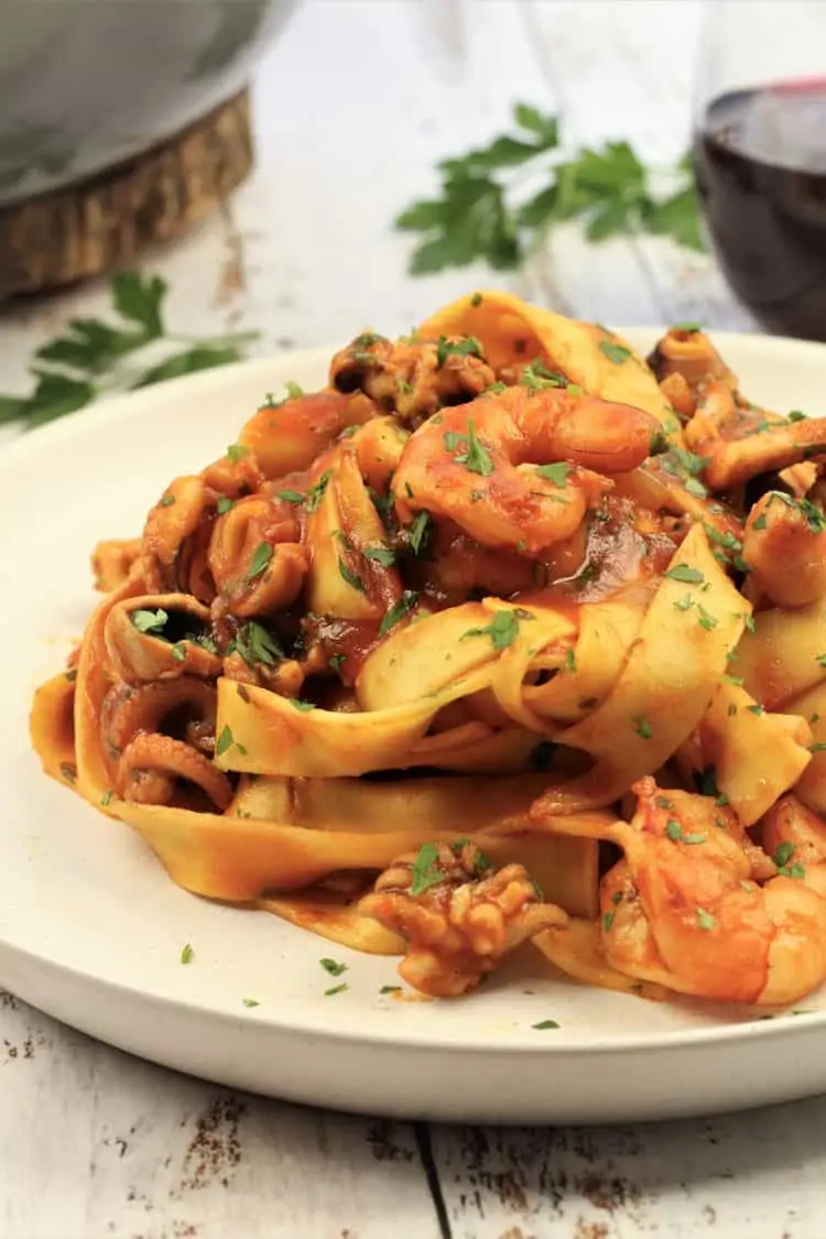 white plate piled with tagliatelle in a seafood tomato sauce