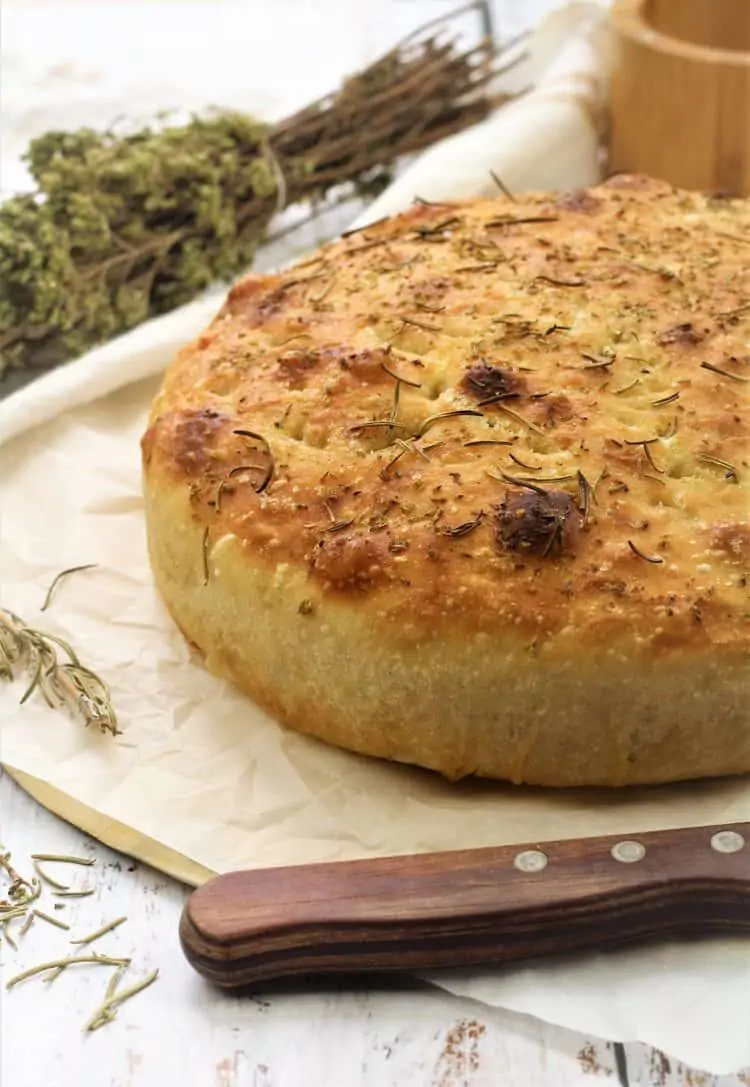 herbed focaccia on wood board with knife and herbs in background