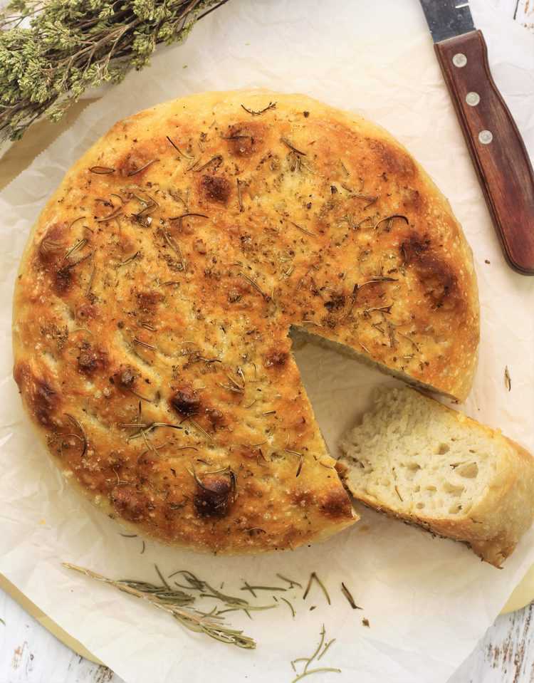 round herbed focaccia bread with wedge cut out of it with knife 