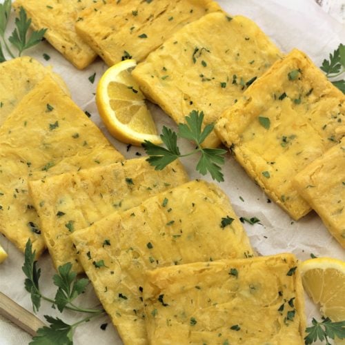 panelle squares on parchment paper covered board with parsley sprigs and lemon wedges