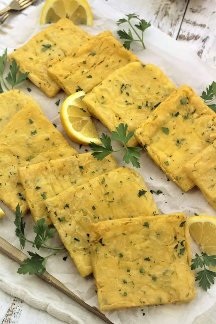 panelle squares on parchment paper covered board with parsley sprigs and lemon wedges