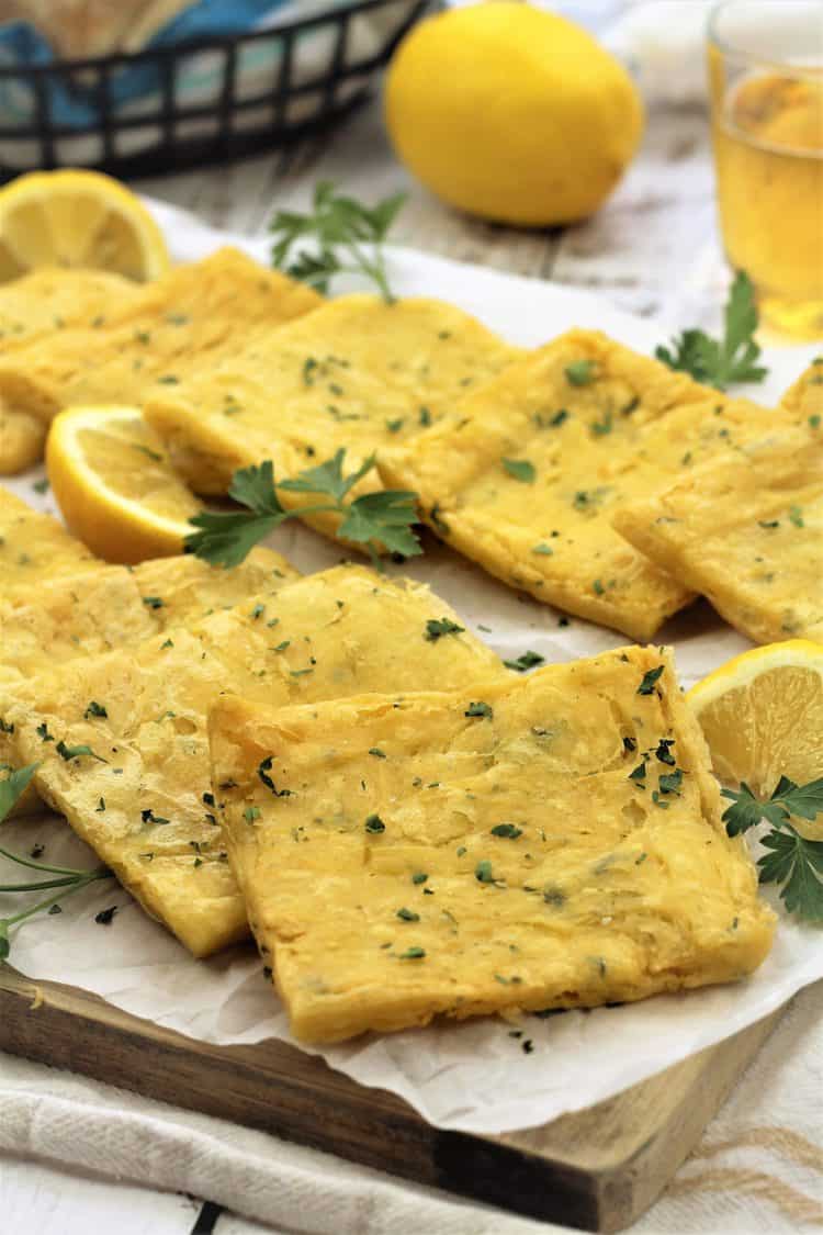 fried panelle squares on wood board with parsley sprigs and lemon wedges