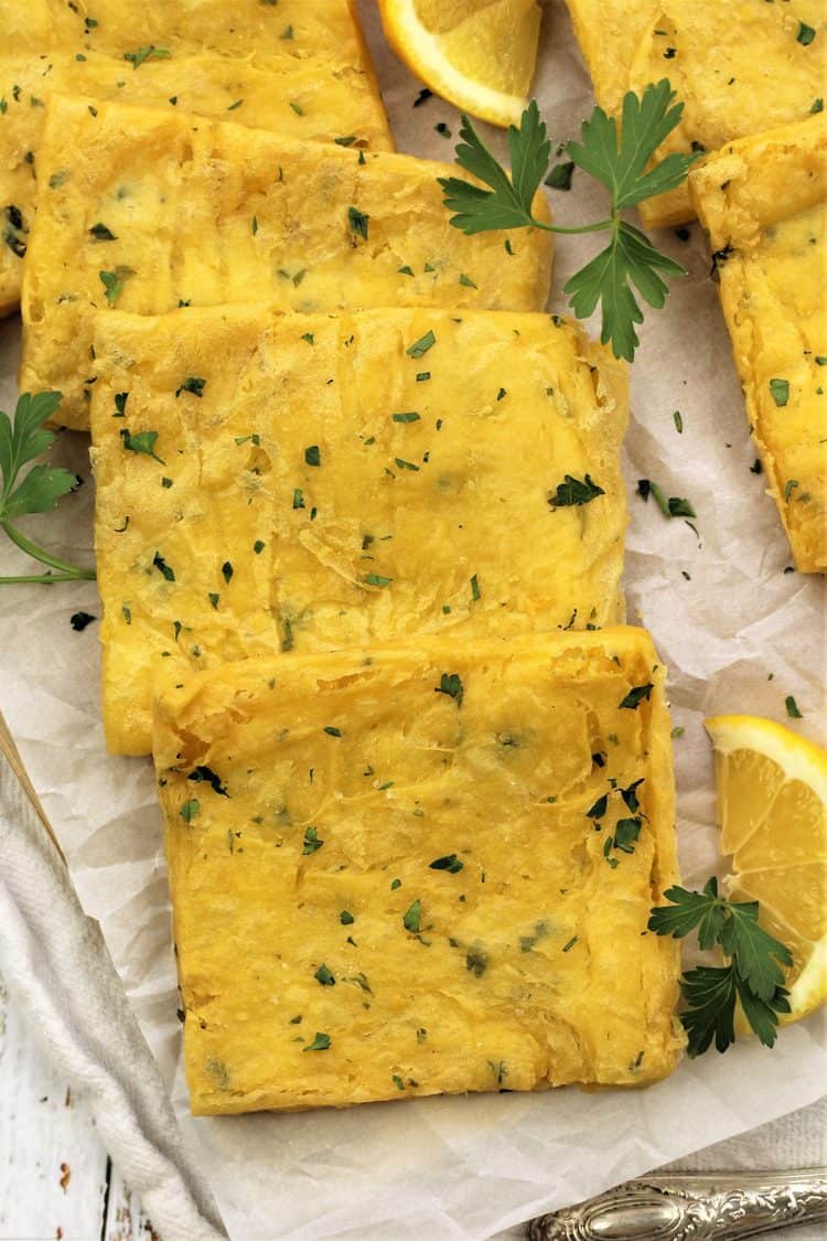 fried panelle squares on parchment paper with parsley sprigs and lemon wedges