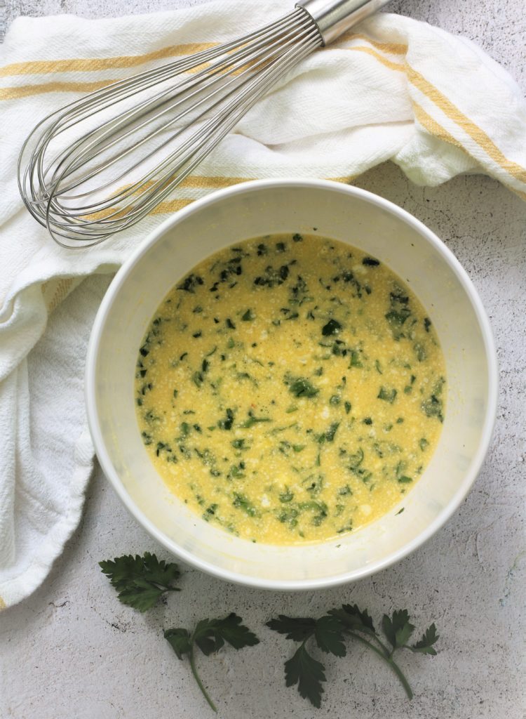 white bowl with beaten eggs, parsley and parmesan cheese with whisk
