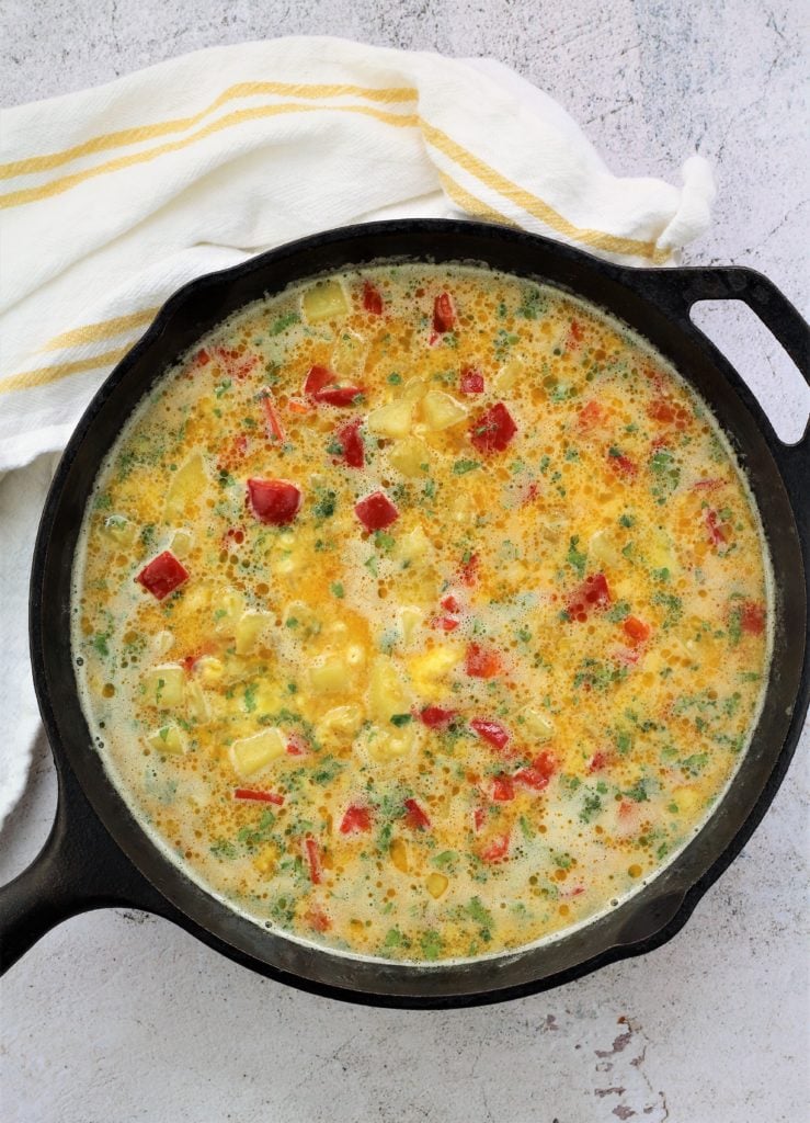 cast iron skillet filled with potato and red pepper frittata mixture