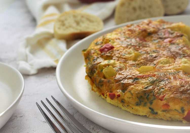 potato and red pepper frittata on round white plate with bread slices 