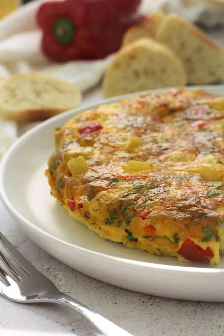 Potato and Red Pepper Frittata on white plate with fork and bread slices behind it