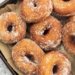 sugar coated doughnuts resting on brown paper on baking sheet