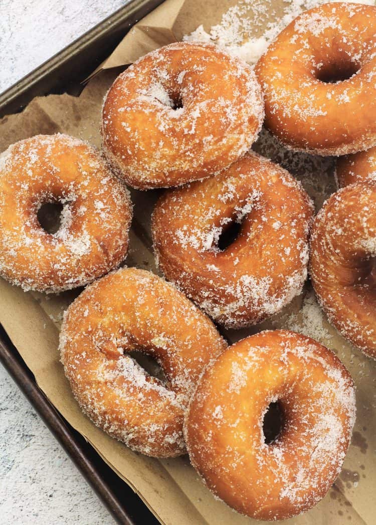 sugar coated doughnuts resting on brown paper on baking sheet