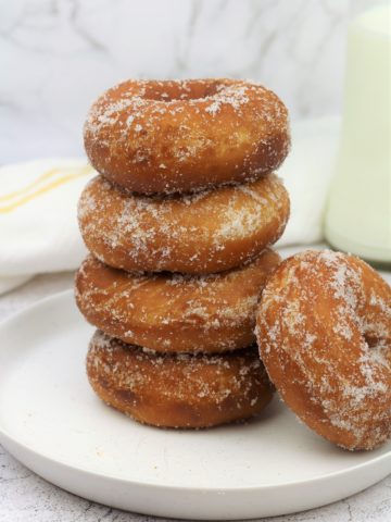 piled sugar coated doughnuts on round plate with one lying on the side