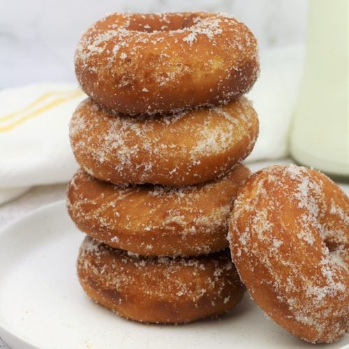 piled sugar coated doughnuts on round plate with one lying on the side