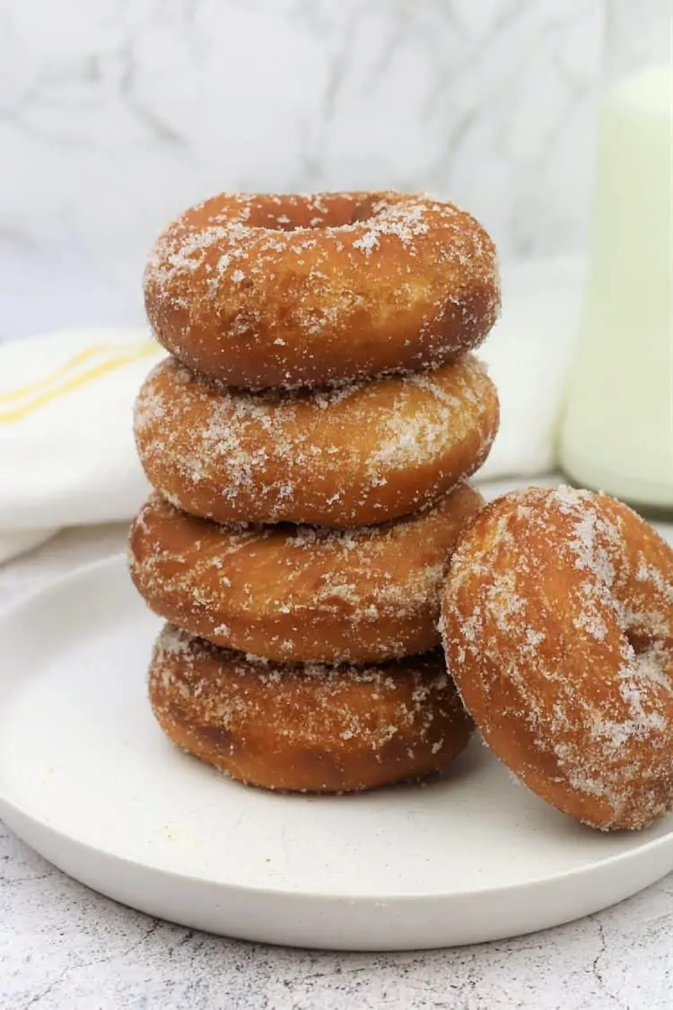 piled sugar coated doughnuts on round plate with one resting on side