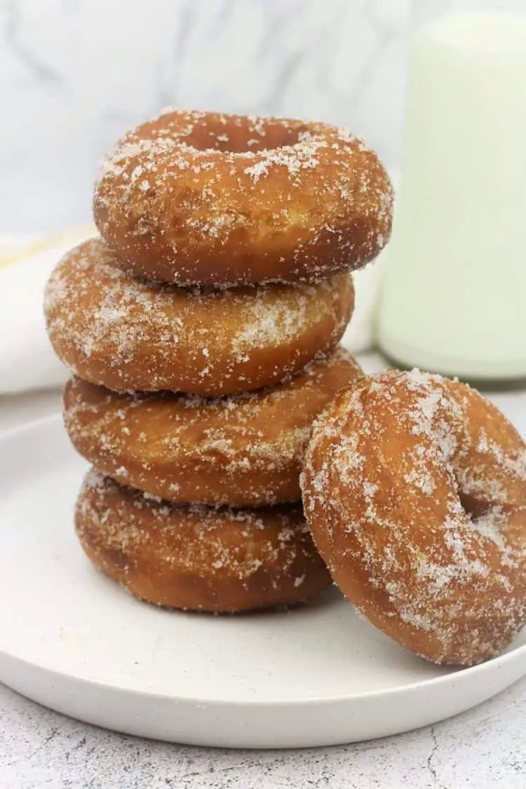 piled sugar doughnuts on round plate with one resting on the side