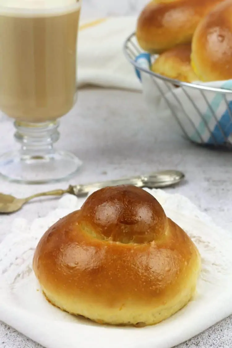 brioche with cup of coffee with milk and basket of brioche in background