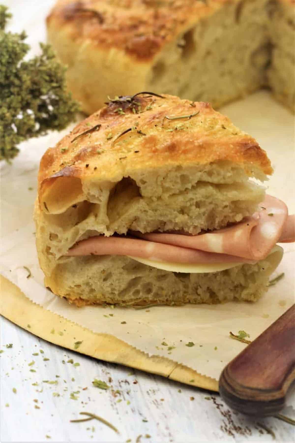 No knead focaccia weddge cut open and stuffed with mortadella and cheese.
