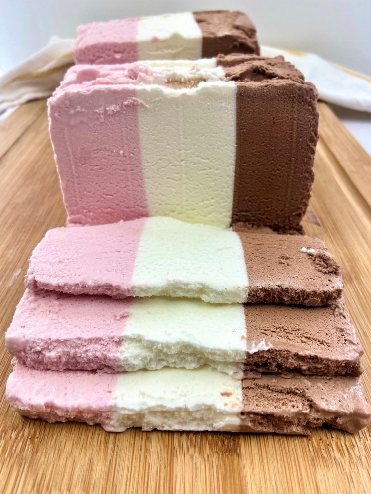 block of Neapolitan ice cream sliced on wood board
