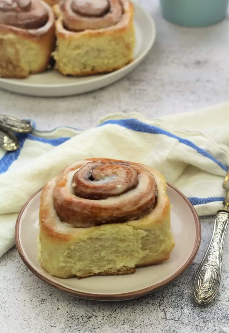 cinnamon roll on plate with plate of buns behind it