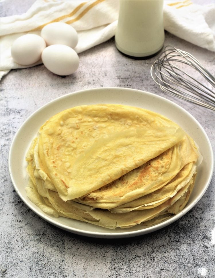 plate of crepes with eggs, milk bottle and whisk