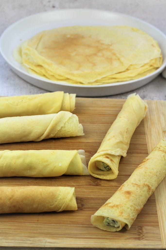 filled rolled crepes on wood board and plate of crepes in background