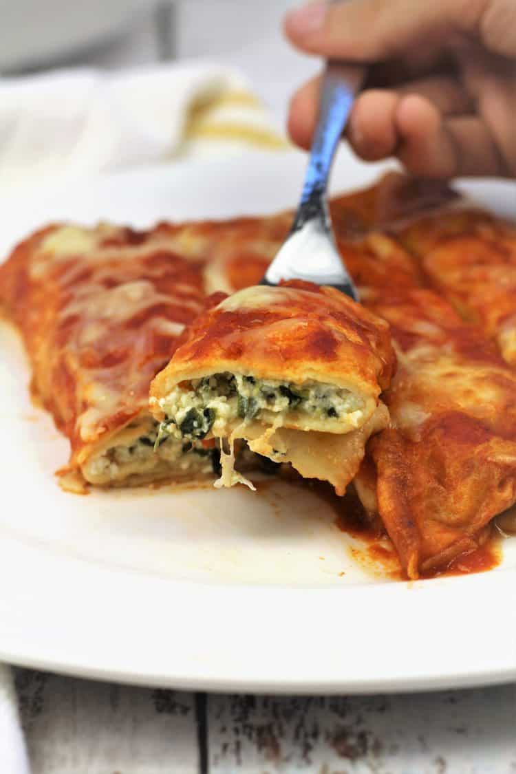 forkful of crepe cannelloni with spinach and ricotta taken from plate full of cannelloni