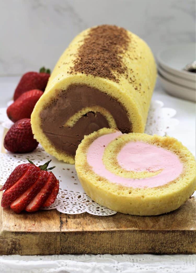 sliced ice cream cake roll with strawberries on wood board
