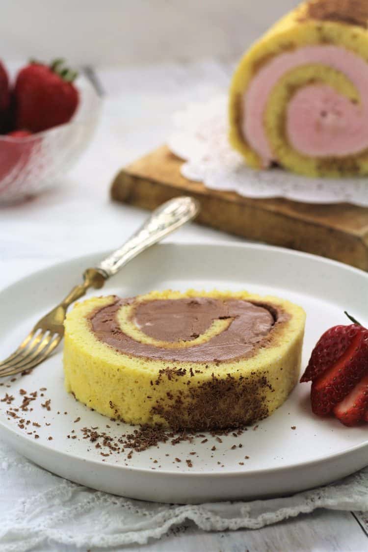 slice of ice cream cake roll on plate with strawberry and grated chocolate