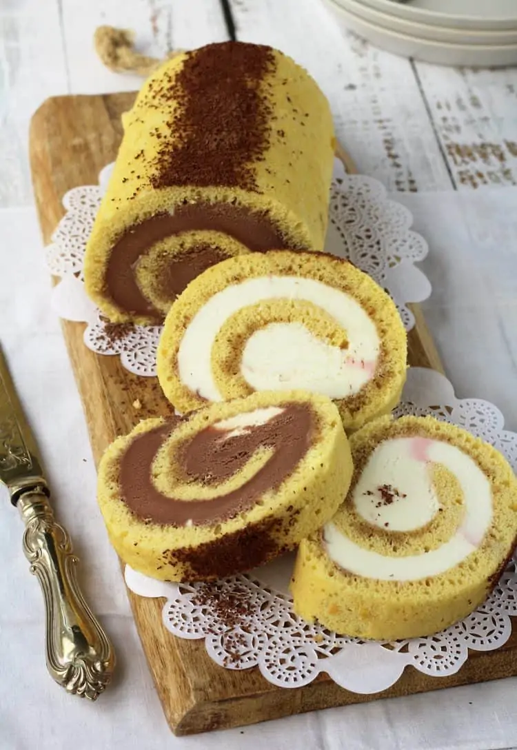 sliced ice cream roll cake with chocolate and vanilla ice cream on wood board with knife on side