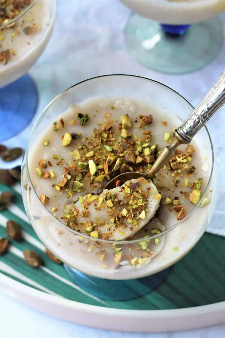 silver spoon in glass filled with almond milk pudding topped with chopped pistachios