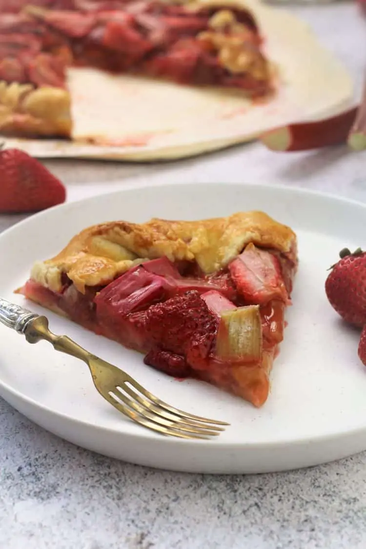 wedge of rhubarb strawberry crostata on white plate with strawberries and fork