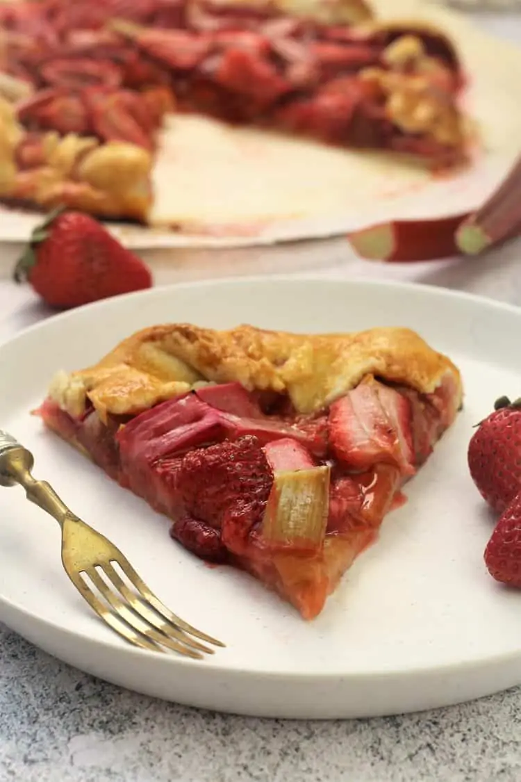 wedge of rhubarb strawberry crostata on white plate with fork and strawberries