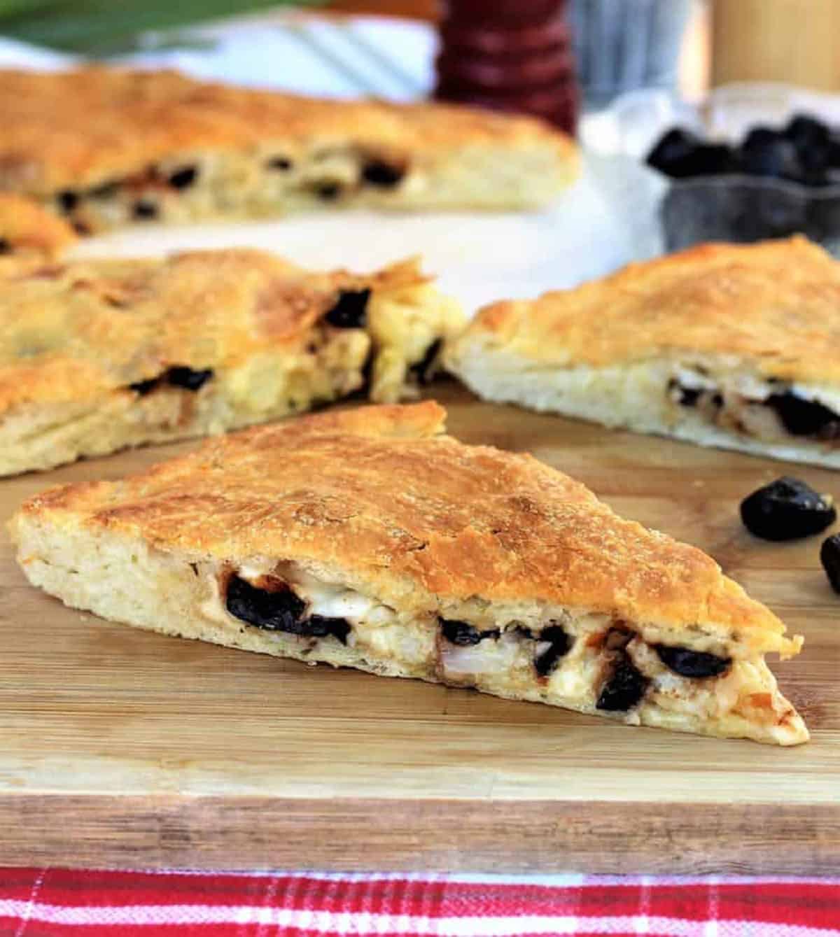 Scacciata with Cauliflower and Black Olives (No Knead Recipe) Cauliflower and black olive filled scacciata cut into wedges on wood board.