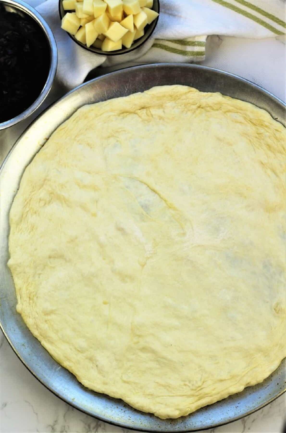 Flattened no knead pizza dough into circular shape on pizza pan.
