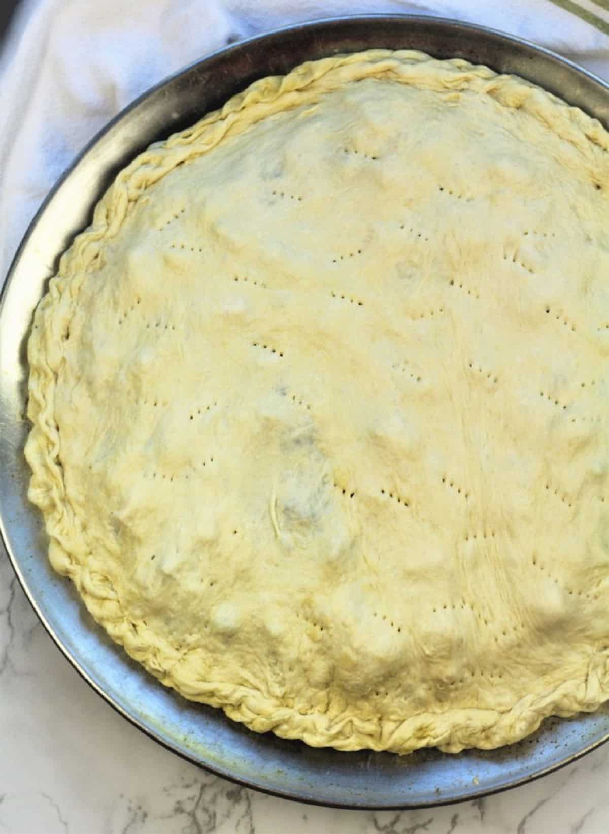Scacciata dough filled with cauliflower and black olive filling on pizza pan brushed with olive oil.