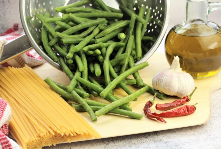 spaghetti, green beans, garlic, red chilis and olive oil bottle on wood board