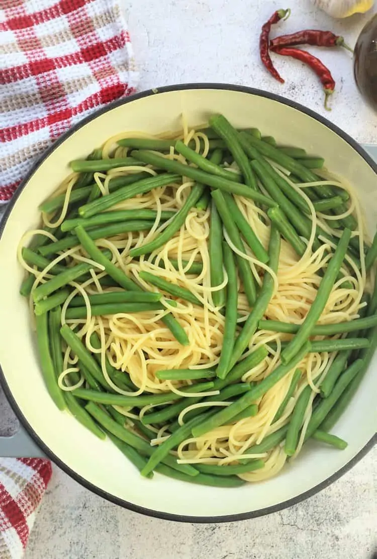 large skillet filled with green beans and spaghetti with red checkered cloth around it