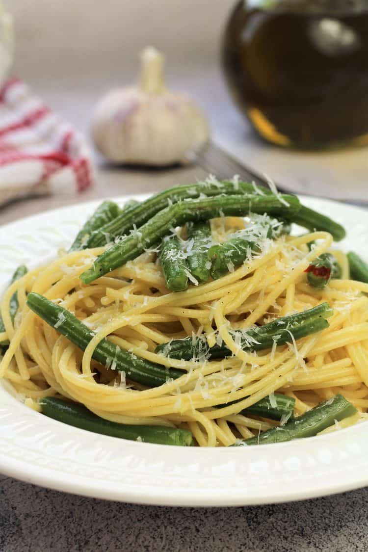 close up of spaghetti with green beans topped with grated cheese in white bowl 