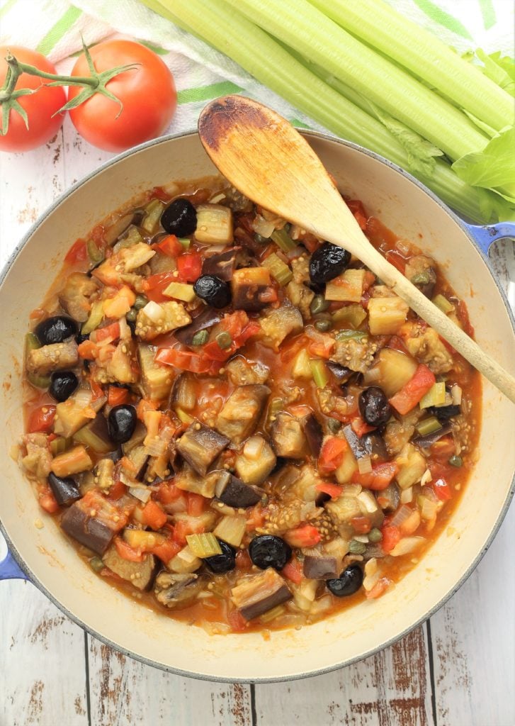 large blue skillet filled with eggplant caponata and tomatoes and celery in background