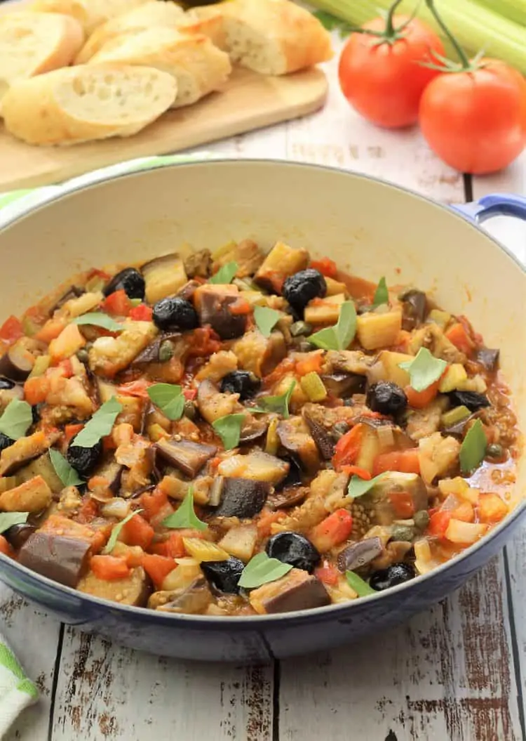 large blue skillet filled with eggplant caponata topped with basil leaves