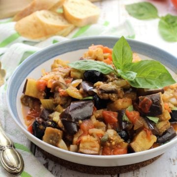 blue rimmed bowl filled with eggplant caponata topped with basil leaves