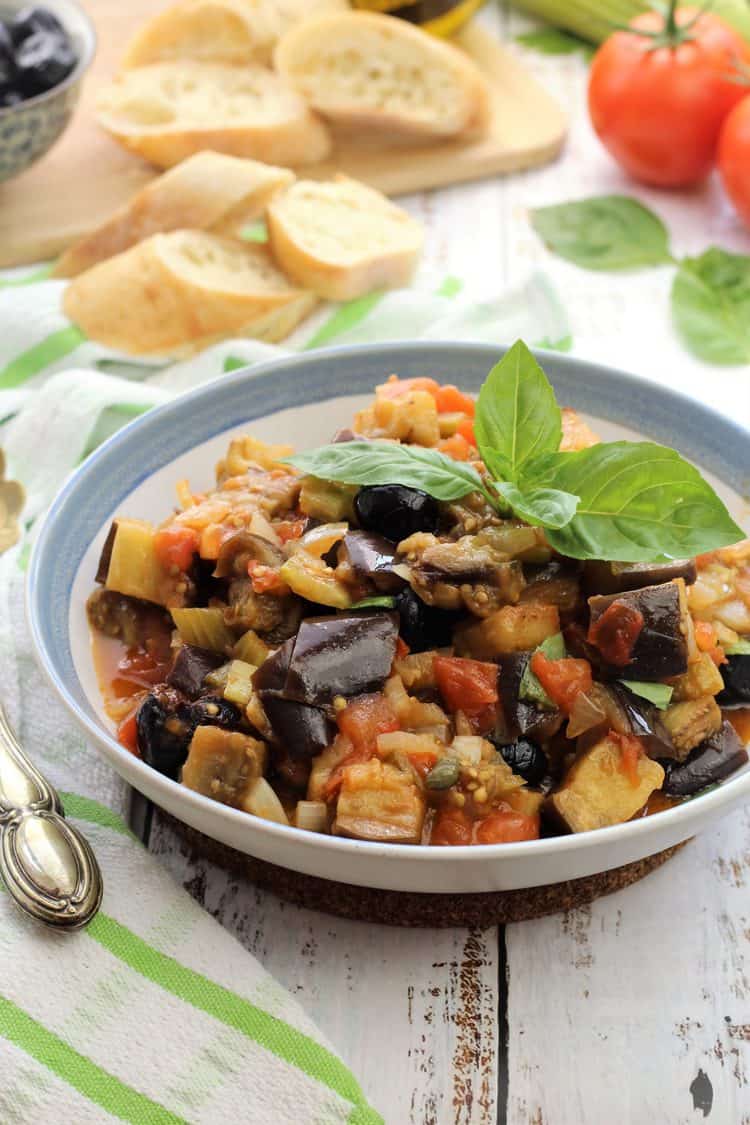 blue rimmed bowl filled with eggplant caponata topped with basil leaves