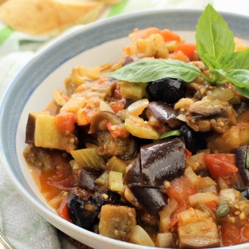 blue rimmed bowl filled with eggplant caponata and basil leaves