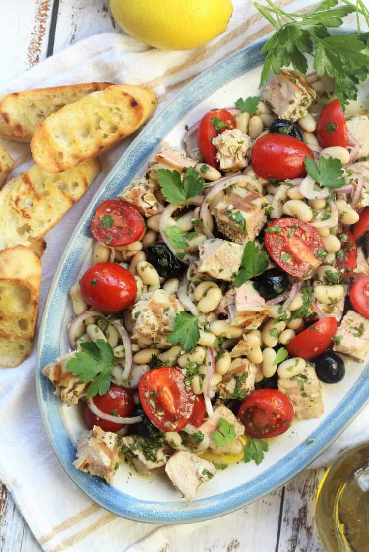 large oval platter filled with grilled tuna, white bean and cherry tomato salad with bread crostini