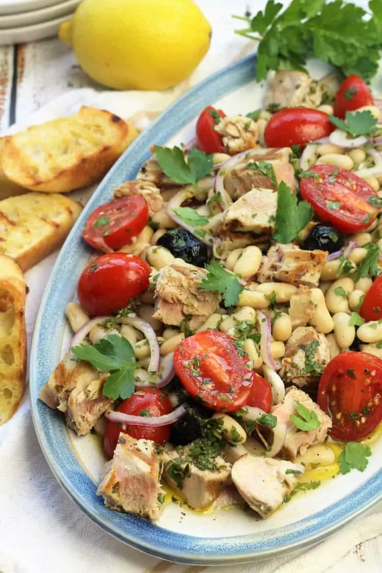 oval platter with grilled tuna and white bean salad surrounded by crusty bread and lemon