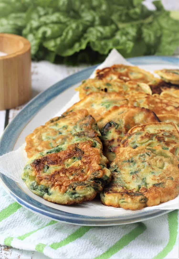 swiss chard frittelle rounds on an blue rimmed oval plate with chard leaves in background